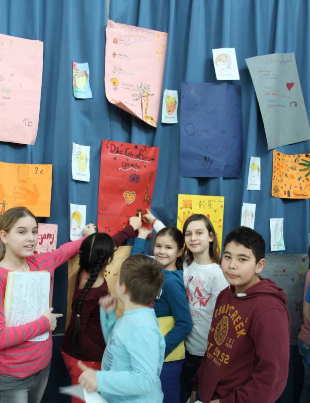 Eine Gruppe von Kindern steht vor einer blauen Wand mit Giraffen-Postern.