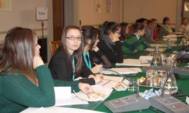 Eine Gruppe junger Leute sitzt an einem Tisch mit Mikrofonen bei einer Konferenz.