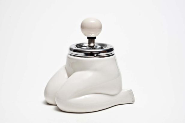 Ein weißer Aschenbecher in Form einer knienden Frau mit einem Chromaufsatz.