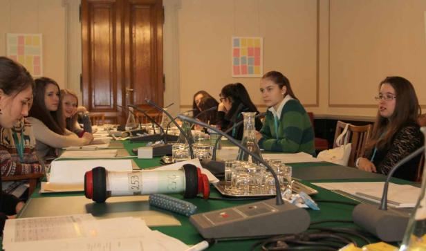 Eine Gruppe junger Frauen sitzt an einem Tisch mit Mikrofonen bei einer Konferenz.