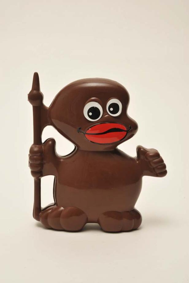 Eine braune Kunststofffigur mit großen Augen und roten Lippen hält einen Speer.