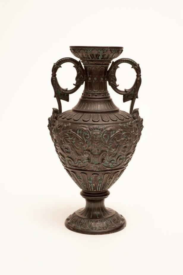 Eine verzierte, dunkle Amphore mit zwei Henkeln steht vor einem weißen Hintergrund.