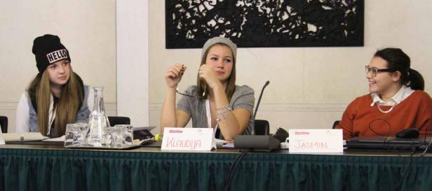 Drei junge Frauen sitzen an einem Tisch mit Namensschildern, darunter Klaudija und Jasmin.