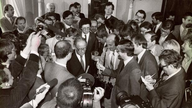 Eine Menschenmenge umringt eine Person, die im Zentrum steht und von Reportern und Kameras umgeben ist.