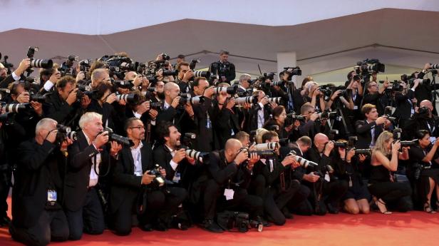 Eine große Gruppe von Fotografen kniet und steht auf einem roten Teppich und fotografiert.
