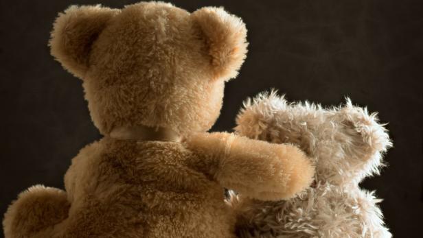 Zwei Teddybären sitzen Rücken an Rücken vor einem dunklen Hintergrund.