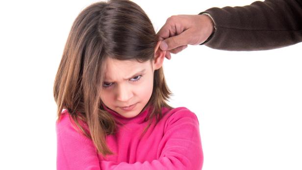 Ein Mädchen blickt grimmig, während ein Erwachsener an ihrem Ohr zieht.