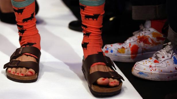 Nahaufnahme von Füßen in Sandalen mit Socken mit Stiermotiv und bemalten Turnschuhen.