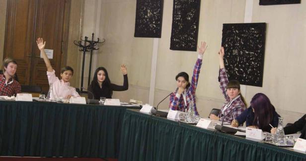 Eine Gruppe junger Leute sitzt an einem Tisch und hebt die Hände.