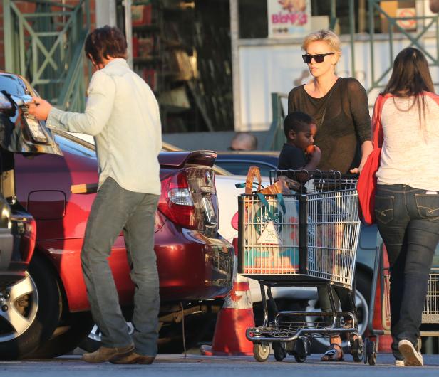 Charlize Theron schiebt einen Einkaufswagen mit ihrem Kind zum Auto.
