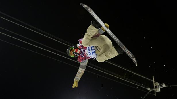 Ein Snowboarder führt einen Trick in der Luft vor dunklem Hintergrund aus.