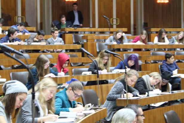 Schüler sitzen in einem Klassenzimmer oder Hörsaal und schreiben an ihren Tischen.