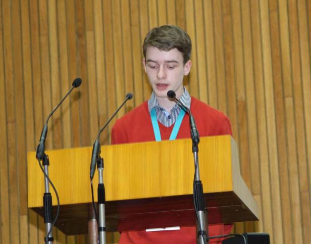 Ein junger Mann hält eine Rede an einem Rednerpult mit mehreren Mikrofonen.