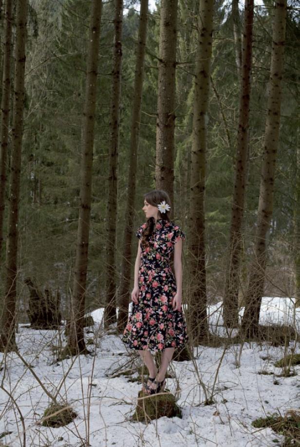 Eine Frau mit einem Blumenkleid steht in einem verschneiten Wald.