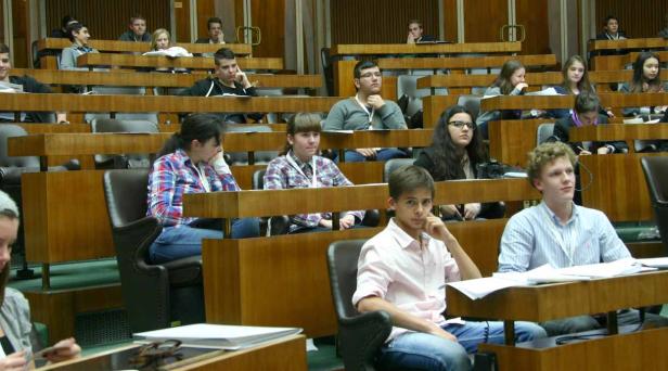 Jugendliche sitzen in einem holzvertäfelten Raum mit Tischen und Stühlen.