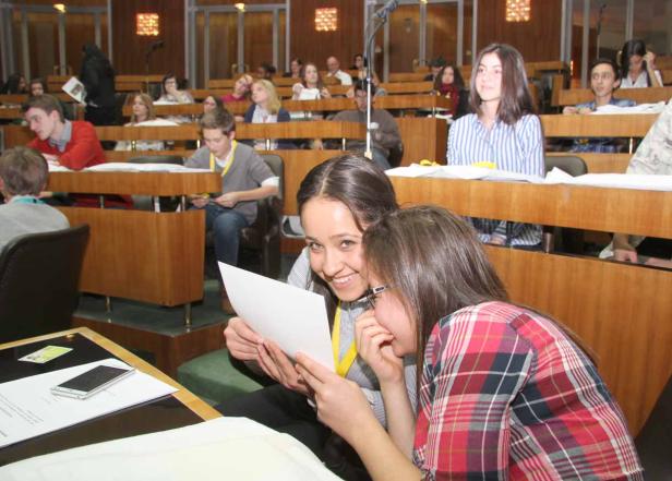 Zwei junge Frauen betrachten lachend ein Blatt Papier in einem Hörsaal.