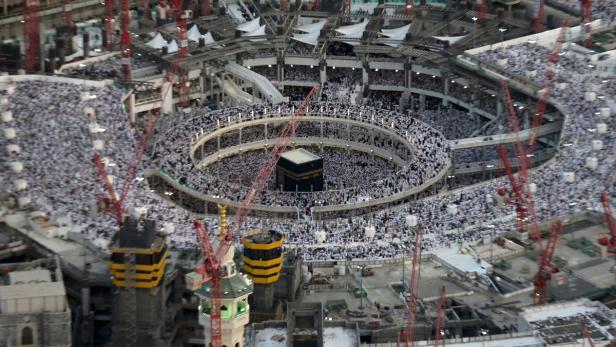Die Kaaba in Mekka, umgeben von einer großen Menschenmenge und Baukränen.