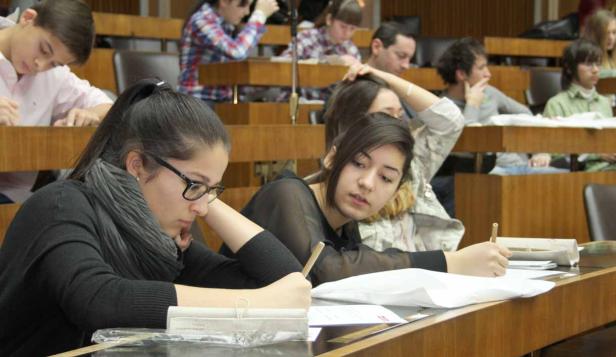 Mehrere Studenten sitzen in einem Hörsaal und schreiben Klausur.
