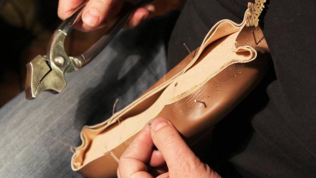 Ein Schuhmacher bearbeitet einen braunen Lederschuh mit einer Zange.