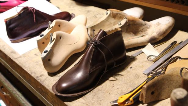 Auf einem Tisch liegen braune Lederschuhe und hölzerne Schuhleisten.