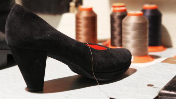 Ein schwarzer Wildleder-Pumps steht vor mehreren Garnrollen.