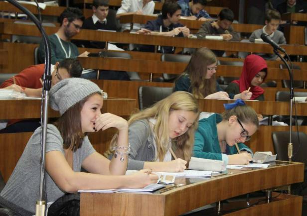 Schüler sitzen in einem Hörsaal und schreiben an ihren Tischen.