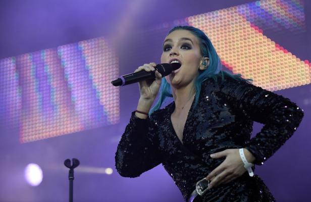 Eine Sängerin mit blauen Haaren tritt auf einer Bühne auf und singt in ein Mikrofon.