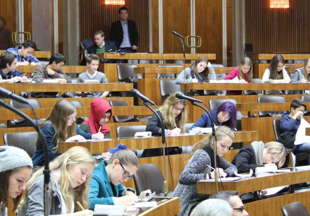 Eine Gruppe von Schülern sitzt in einem holzvertäfelten Raum und schreibt an ihren Tischen.