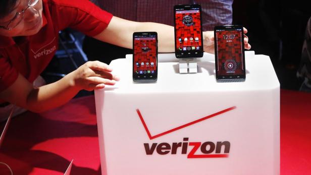 Eine Person präsentiert drei Verizon-Smartphones auf einem Stand mit dem Verizon-Logo.