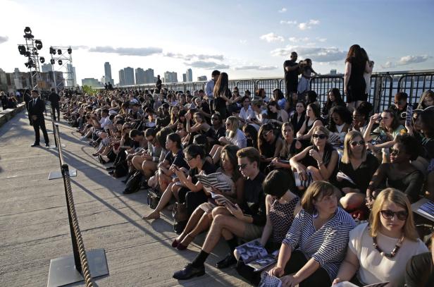 Zahlreiche Zuschauer sitzen bei einer Modenschau im Freien.