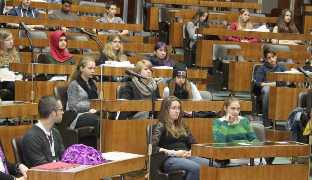 Eine Gruppe junger Leute sitzt in einem holzvertäfelten Raum mit Mikrofonen vor sich.