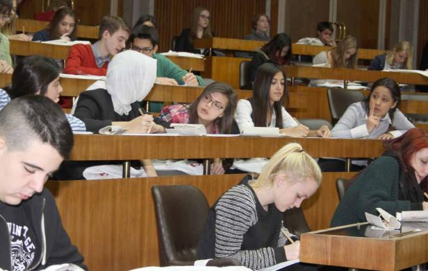 Mehrere Studenten sitzen in einem Hörsaal und schreiben mit Stiften.