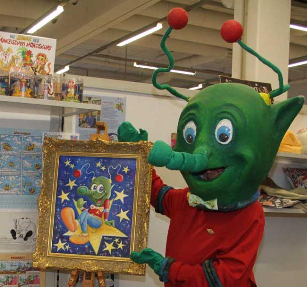 Ein grünes Maskottchen hält ein gerahmtes Bild von sich selbst, sitzend auf einem Stern.