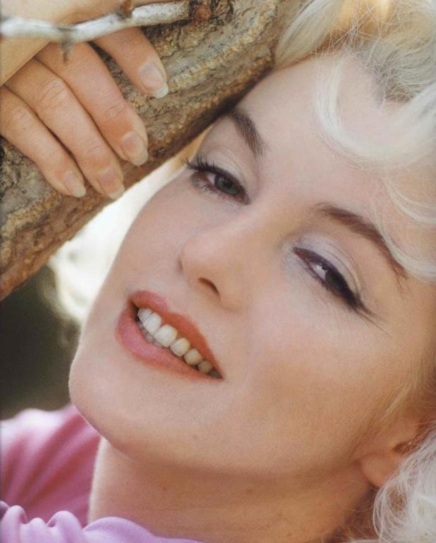 Nahaufnahme einer Frau mit blonden Haaren, die sich an einen Baum lehnt.