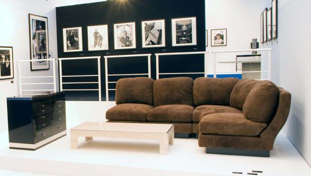 Ein braunes Ecksofa und ein Couchtisch in einem Ausstellungsraum mit Fotografien an der Wand.