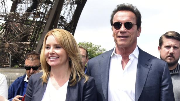 Arnold Schwarzenegger und eine Frau posieren vor dem Eiffelturm.