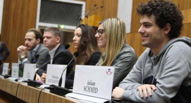 Mehrere Personen sitzen an einem Tisch mit Namensschildern bei einer Konferenz.