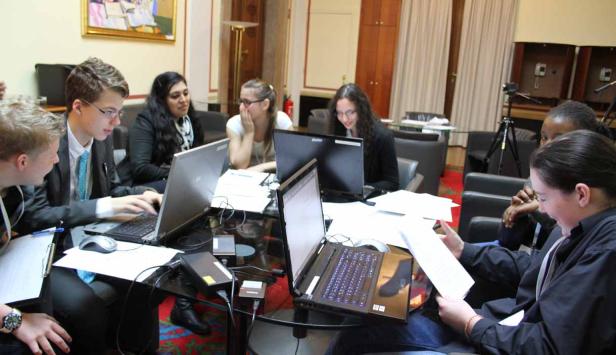 Eine Gruppe junger Leute sitzt an einem Tisch und arbeitet an Laptops.