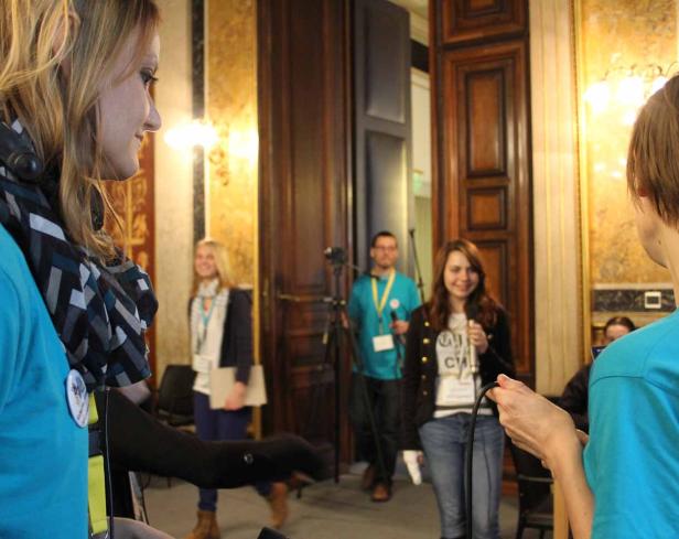 Mehrere Personen stehen in einem Raum mit hohen Türen und sprechen miteinander.