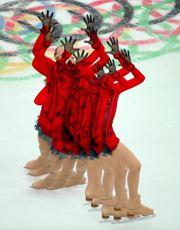 Eine Eiskunstläuferin in einem roten Kostüm mit erhobenen Händen vor dem Hintergrund der olympischen Ringe.