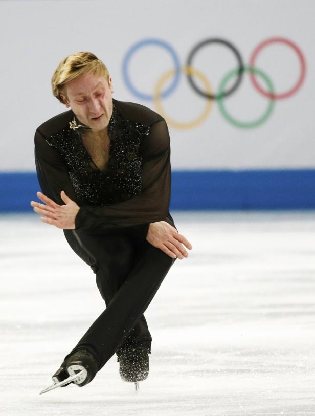 Ein Eiskunstläufer in schwarzer Kleidung läuft vor dem Hintergrund der Olympischen Ringe Schlittschuh.
