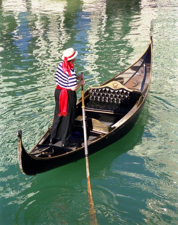 Ein Gondoliere in Venedig steuert seine Gondel durch das Wasser.