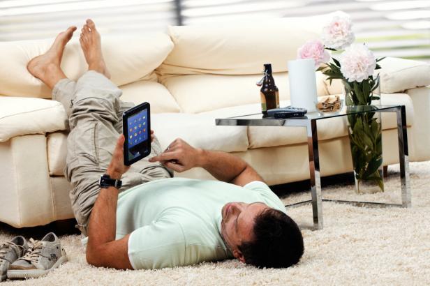 Ein Mann liegt auf einem Teppich und bedient ein Tablet.