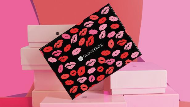 Eine Glossybox mit einem Muster aus roten und rosa Lippenstiftabdrücken auf einem rosa Hintergrund.