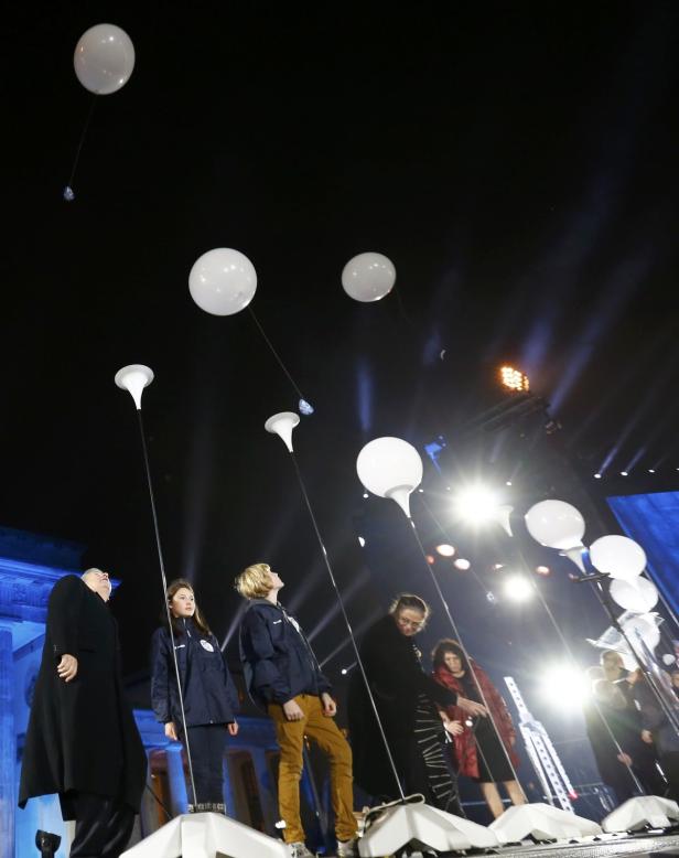 Mehrere Personen stehen auf einer Bühne und schauen zu weißen Ballons auf.