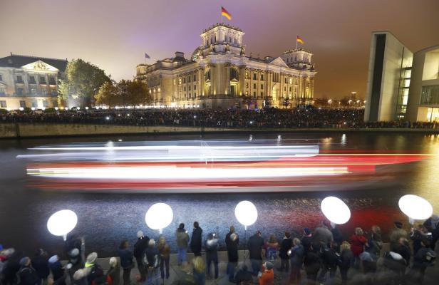 Der Reichstag in Berlin bei Nacht, beleuchtet und mit Menschenmassen am Ufer der Spree.