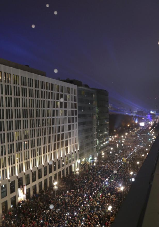 Eine Menschenmenge versammelt sich nachts auf einer beleuchteten Straße in Berlin.