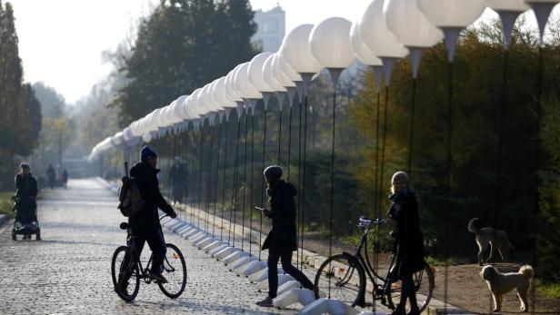 Menschen spazieren und fahren Fahrrad in einem Park mit einer Installation aus weißen Kugeln.