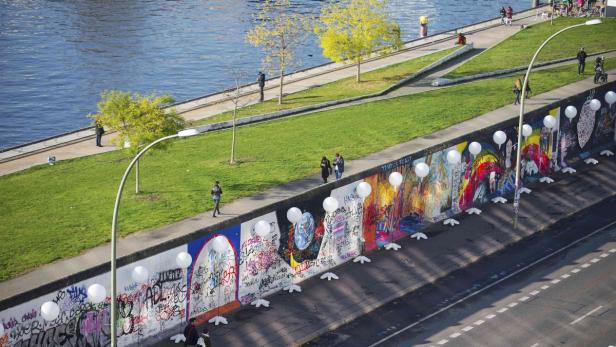 Ein Abschnitt der Berliner Mauer mit Graffiti und weißen Ballons entlang einer Straße.