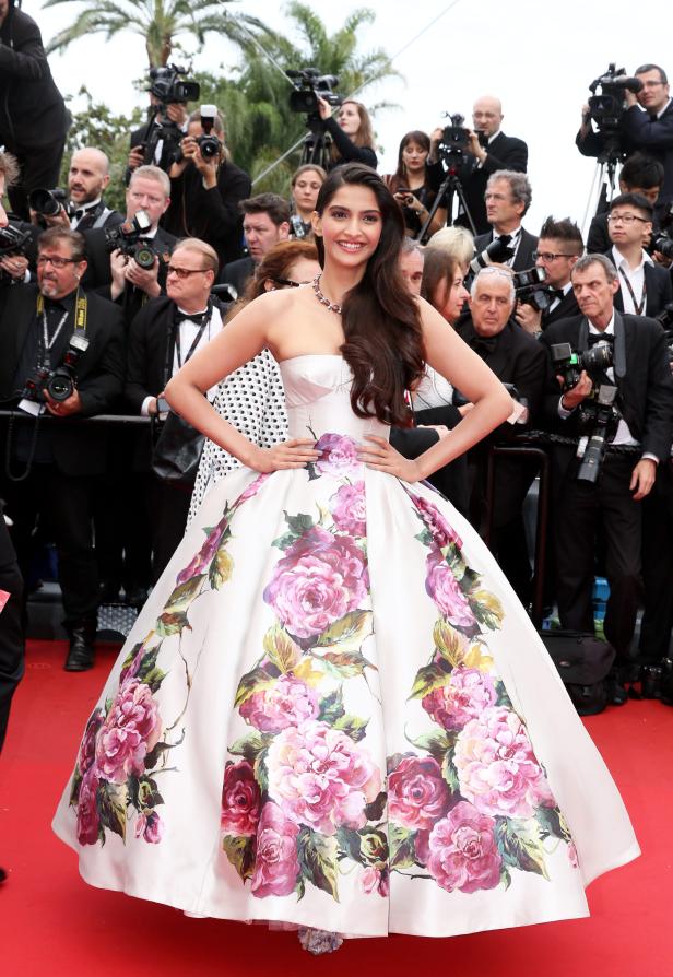 Sonam Kapoor posiert auf dem roten Teppich in einem weißen, blumengemusterten Kleid.